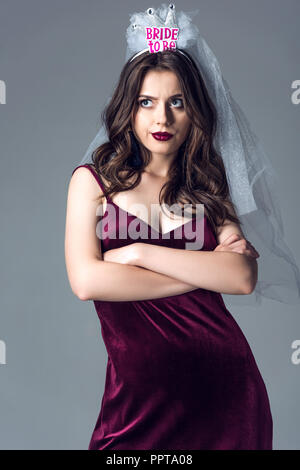 confused future bride in veil for bachelorette party with crossed arms looking up isolated on grey Stock Photo