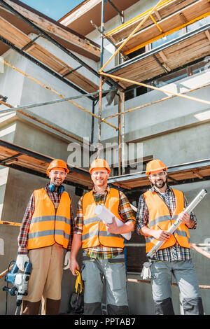 group of smiling equipped builders looking at camera at construction site Stock Photo
