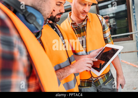 close-up shot of group of builders using digital tablet at construction site Stock Photo