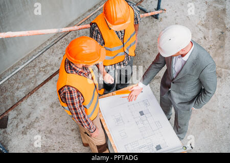 high angle view of builders and architect discussing blueprint at construction site Stock Photo