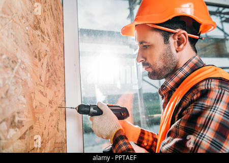 side view of handsome builder using handheld electric drill Stock Photo