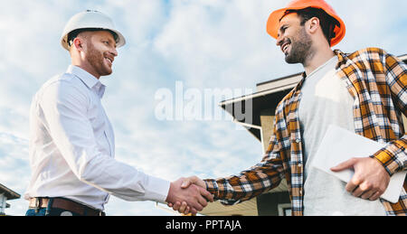 bottom view of smiling architects shaking hands in front of construction site Stock Photo