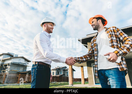 smiling architects shaking hands in front of construction site Stock Photo