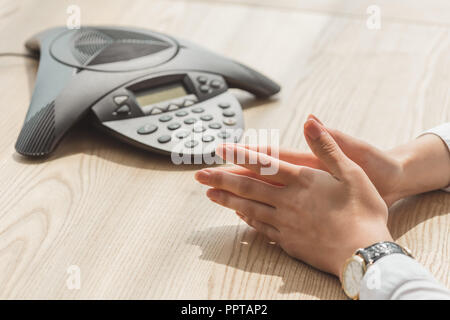cropped shot of businesswoman sitting in front of conference phone on wooden table Stock Photo