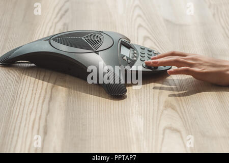 cropped shot of businesswoman pushing button of speakerphone on wooden table Stock Photo