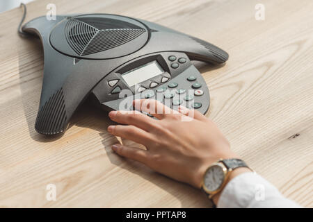 cropped shot of businesswoman pushing button of speakerphone on wooden table at office Stock Photo