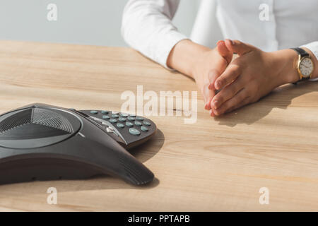 cropped shot of businesswoman in white shirt sitting in front of conference phone on table at office Stock Photo