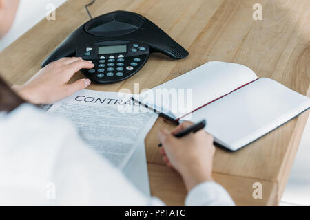 cropped shot of businesswoman with contract pushing button of conference phone on table at office Stock Photo