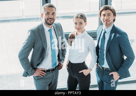 group of smiling young business people standing at modern office and looking at camera Stock Photo
