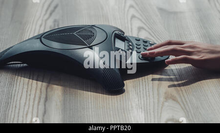 cropped shot of businesswoman pushing button of speakerphone on wooden table Stock Photo