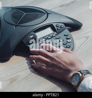 cropped shot of businesswoman pushing button of speakerphone on wooden table at office Stock Photo