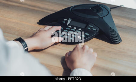 cropped shot of businesswoman pushing button of conference phone on table at office Stock Photo