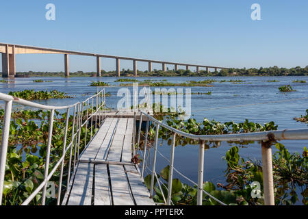 Rustic wooden footpath bridge over water, small dock pier, Rio (River) Paraguay, Puente (Bridge) Remanso Castillo on the background, M.R.A., Paraguay Stock Photo