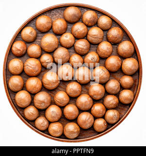 macadamia nuts in shells on on a round wooden tray isolated on white Stock Photo
