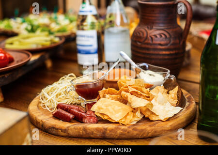 Delicious snacks for beer. Hot hunting sausages on the cheese next to the chips and sauces on the board. Stock Photo