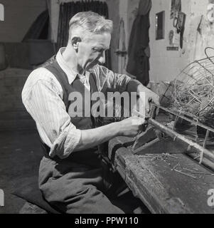1950s, historical, male craftsman inside an outbuilding at a farm sitting working at wooden workbench making some form of large brush, England, UK. Stock Photo