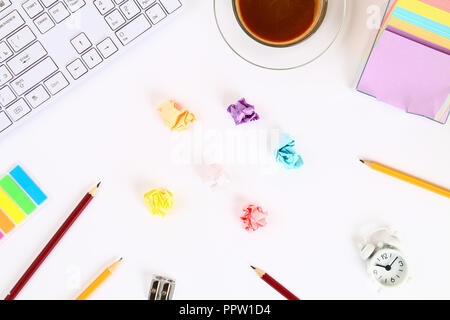 Crumpled multicolored sheets of paper on a white desktop next to a coffee mug and a keyboard. Top view, flat layout. Copy the space Stock Photo