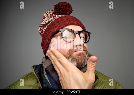 Funny mature man wearing glasses and warm clothes looking at camera checking his bristle. Stock Photo