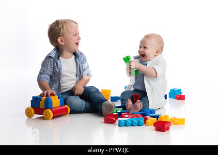 A two year old boy playing with his seven month old baby brother playing with building blocks. Shot in the studio on a white, seamless backdrop. Stock Photo