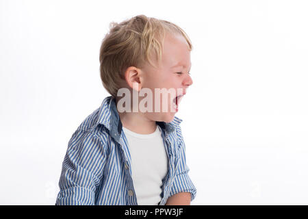 A profile view of a two year old boy crying. Shot in the studio on a white, seamless backdrop. Stock Photo