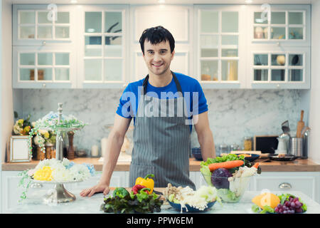 Handsome man cooking at home preparing salad in kitchen. Healthy eating, vegetarian food, diet and people concept Stock Photo