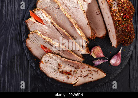 Slices of delicious roasted ham rubbed with spices: paprika, chili flakes, coriander, ground black pepper, garlic cloves, ginger, served on a black st Stock Photo