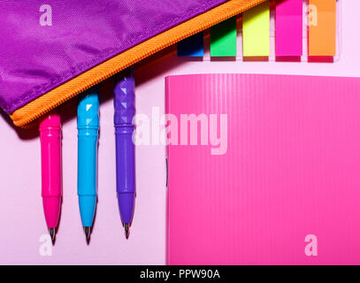 Pink notebook and purple pencil case with pens on the pink background. Flat lay, top view. place for text. Stock Photo