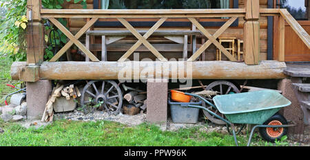 Under the porch of a wooden village shed is stored household utensils, firewood, basins and a wheelbarrow. Panoramic shot in rustic style Stock Photo