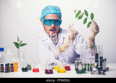 Crazy scientist pours the liquid from a tube to other tube doing an experiment with creepy face emotion, isolated on a white background. Stock Photo