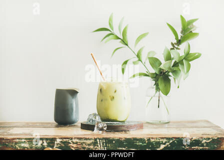 Iced matcha latte with milk pouring from pitcher, horizontal composition