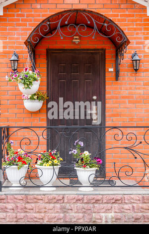 A beautiful porch in a rich house with black door, red brick wall and flower pots. Stock Photo