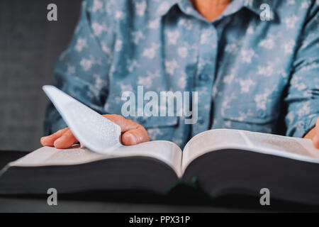 Old woman flipping through pages of book. Grandmother with Bible. Concentrated elderly pensioner with wrinkles on hands looking for information in the library Stock Photo