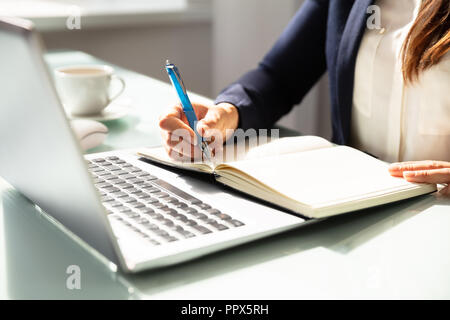 Close-up Of A Businesswoman's Hand Writing Note With Pen In Diary Over Desk Stock Photo