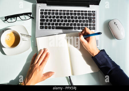 Close-up Of A Businesswoman's Hand Writing Note With Pen In Diary Over Desk Stock Photo