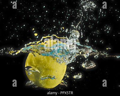 A lemon splashing into the water with black background and bubbles. Stock Photo
