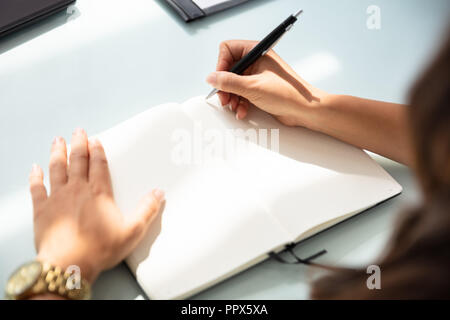Close-up Of A Businesswoman Writing In Notebook With Pen Over Desk Stock Photo