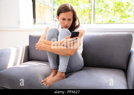Young Woman Sitting On Sofa Using Smartphone Stock Photo