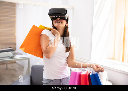 Smiling Young Woman Using Virtual Reality Device For Shopping Experience At Home Stock Photo
