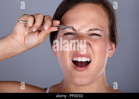 Close-up Of A Young Woman Having Pain While Plucking Eyebrow Hair With Tweezers Stock Photo