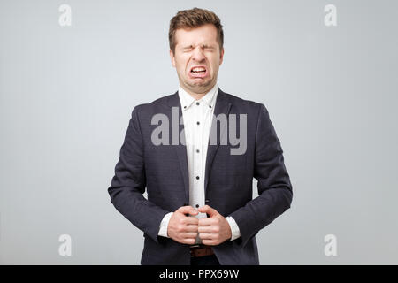 A young man in suit with a grimace of disgust on his face. He puts out his tongue. Stock Photo