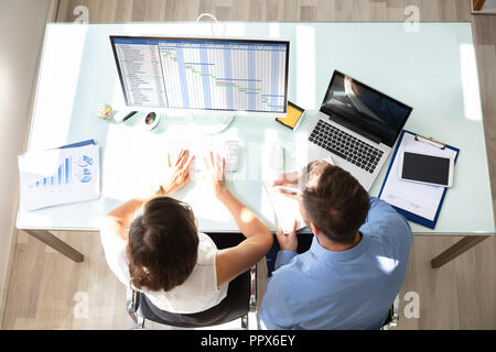 Overhead View Of Two Businesspeople Analyzing Gantt Chart On Computer In Office Stock Photo
