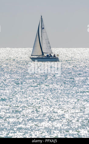 Single person yacht sailing at sea with the morning sun sparkling in the ocean, in the UK.