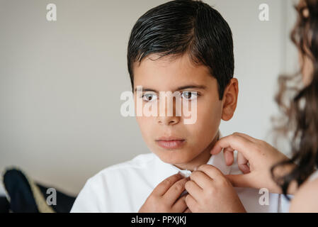 Young boy getting ready for celebration. Her sister is helping him Stock Photo