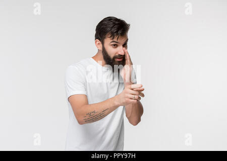 Secret, gossip concept. Young man whispering a secret behind his hand. Businessman isolated on white studio background. Young emotional man. Human emotions, facial expression concept. Stock Photo