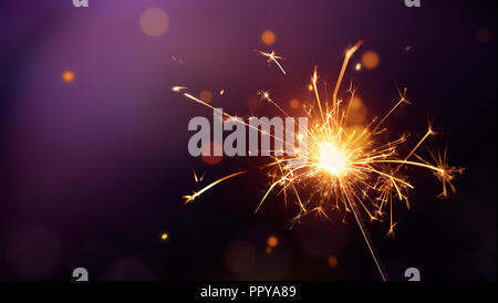 Glittering burning sparkler on purple background Stock Photo