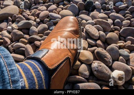 A tan shoe walking on colourful pebbles on Sidmouth beach. Stock Photo