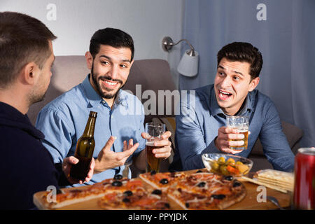 Friendly cheerful positive meeting in men company over beer with pizza at home Stock Photo