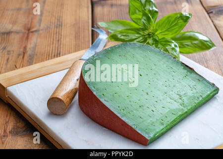 Cheese collection, piece of Dutch green pesto hard cheese with fresh basil close up Stock Photo