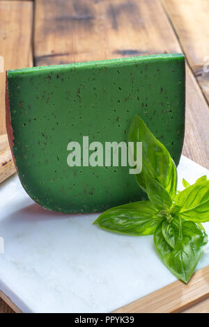 Cheese collection, piece of Dutch green pesto hard cheese with fresh basil close up Stock Photo