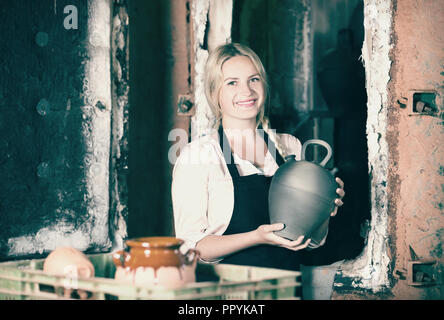 Woman sculptor in black apron holding black glazed spot Stock Photo